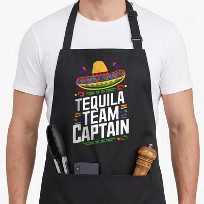 Tablier de cuisine noir avec un sombrero coloré et le texte Tequila Team Captain imprimé en blanc au centre.