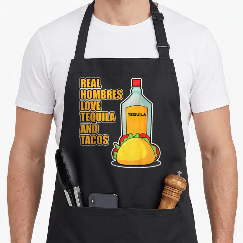 Tablier de cuisine noir avec une illustration dune bouteille de tequila et un taco jaune vert rouge et le texte Real Hombres Love Tequila and Tacos