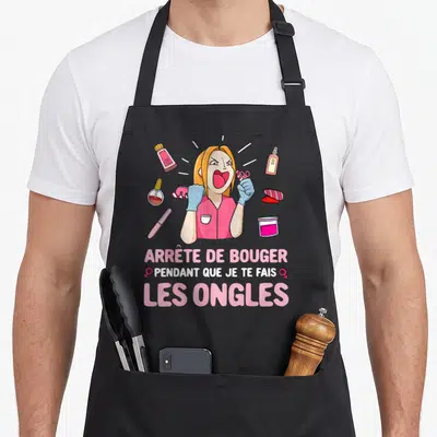 Tablier de cuisine noir avec une esthéticienne aux cheveux blonds criant et tenant des ciseaux, entourée d'outils de manucure roses.