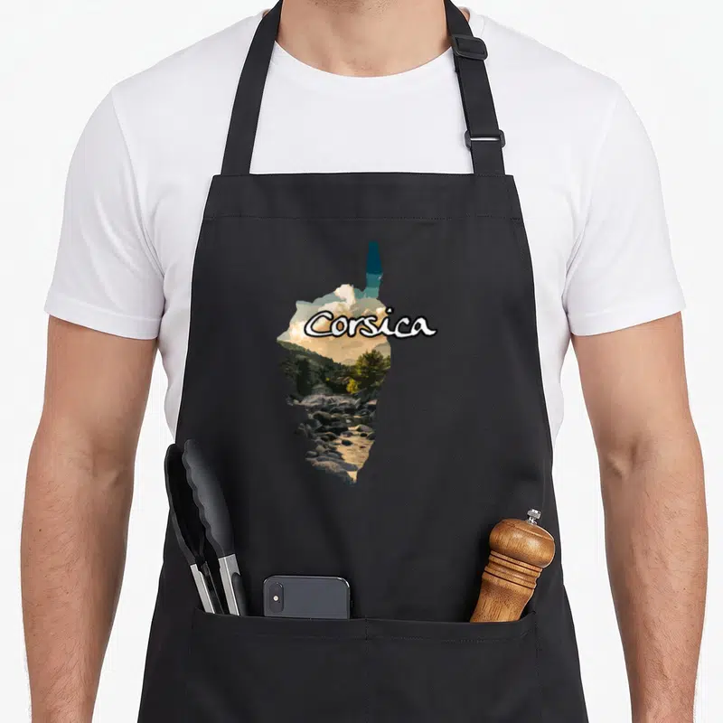 Tablier de cuisine noir avec une silhouette d'île intégrant un paysage de rochers, d'arbres et le texte Corsica en blanc.