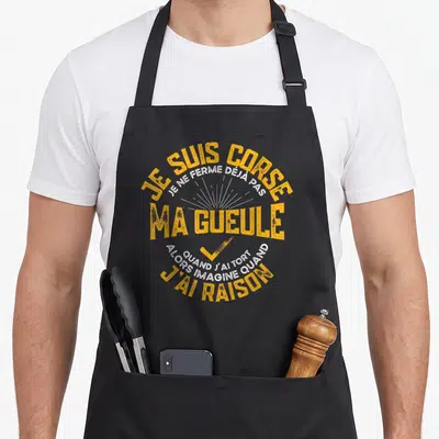 Tablier de cuisine noir avec inscription Je Suis Corse Ma Gueule en orange et blanc.