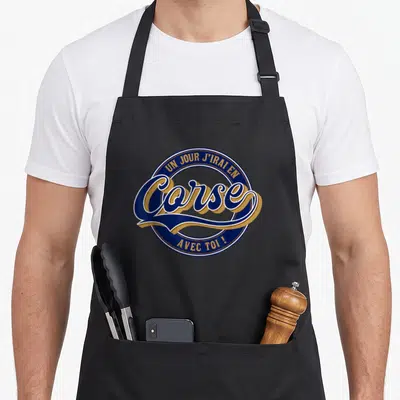 Tablier de cuisine noir avec un logo circulaire bleu et or portant linscription Un jour jirai en Corse avec toi