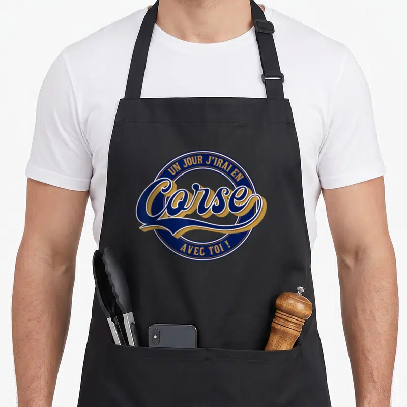 Tablier de cuisine noir avec un logo circulaire bleu et or portant linscription Un jour jirai en Corse avec toi