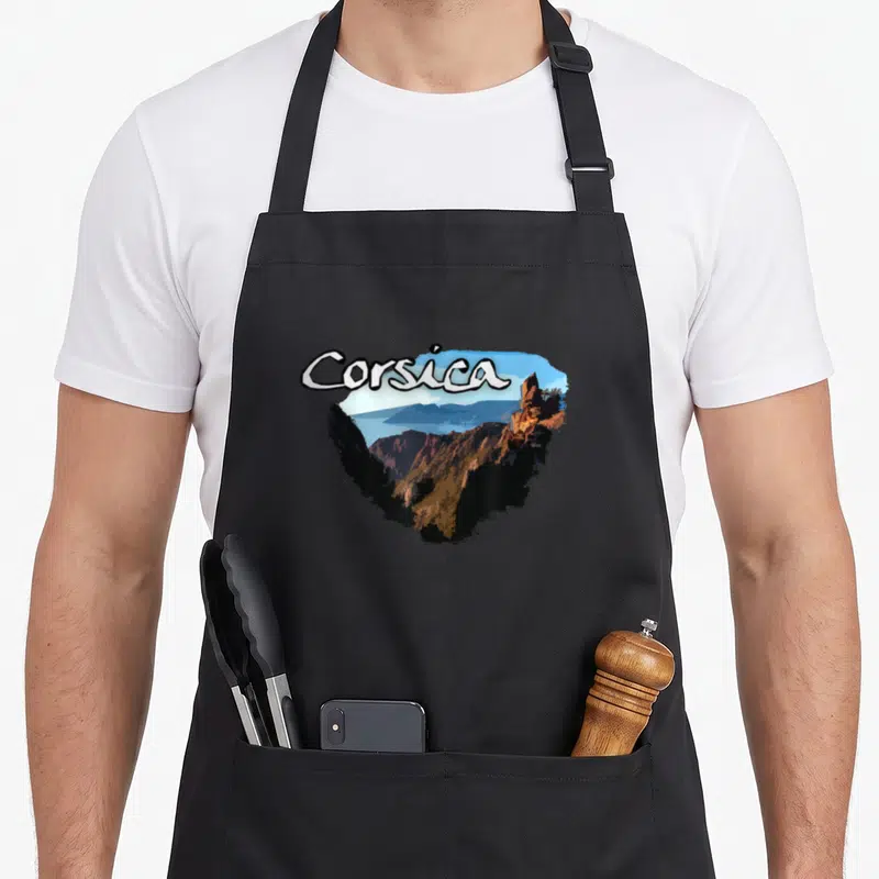 Tablier de cuisine noir avec illustration Corsica montrant des falaises rocheuses et une vue sur la mer bleue.