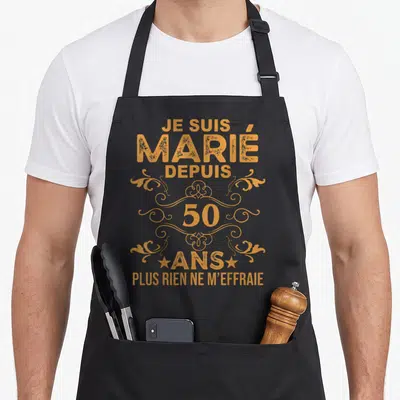 Tablier de cuisine noir avec inscription Je suis marié depuis 50 ans plus rien ne m'effraie en lettres dorées ornées de volutes.
