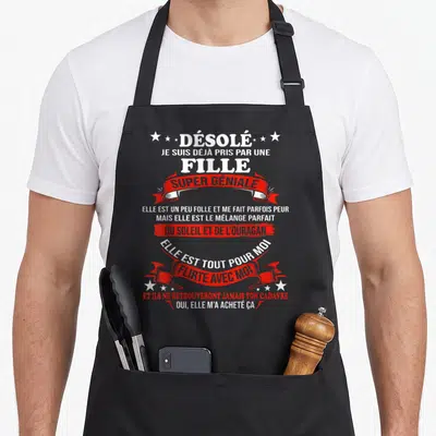 Tablier de cuisine noir avec texte blanc et rubans rouges proclamant être pris par une fille super géniale.
