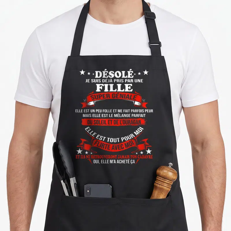 Tablier de cuisine noir avec texte blanc et rubans rouges proclamant être pris par une fille super géniale.