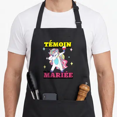 Tablier de cuisine noir avec une licorne colorée en pose dab tenant un verre de vin rouge.