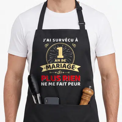 Tablier de cuisine noir avec l'inscription 1 an de mariage plus rien ne me fait peur et des anneaux dorés.