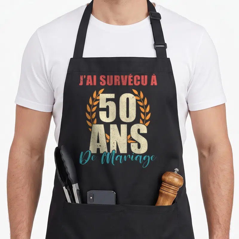 Tablier de cuisine noir avec l'inscription Jai survécu à 50 ans de mariage entouré de lauriers orange et beige.