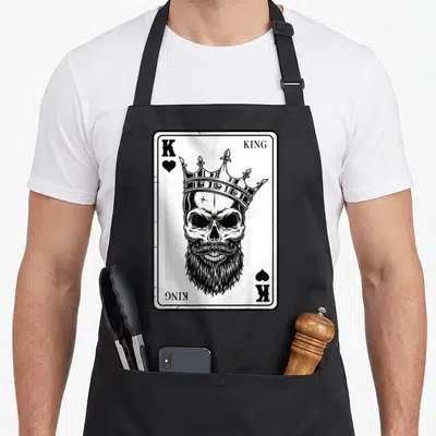 Tablier de cuisine noir avec illustration carte à jouer King Skull couronné et barbu en noir et blanc.