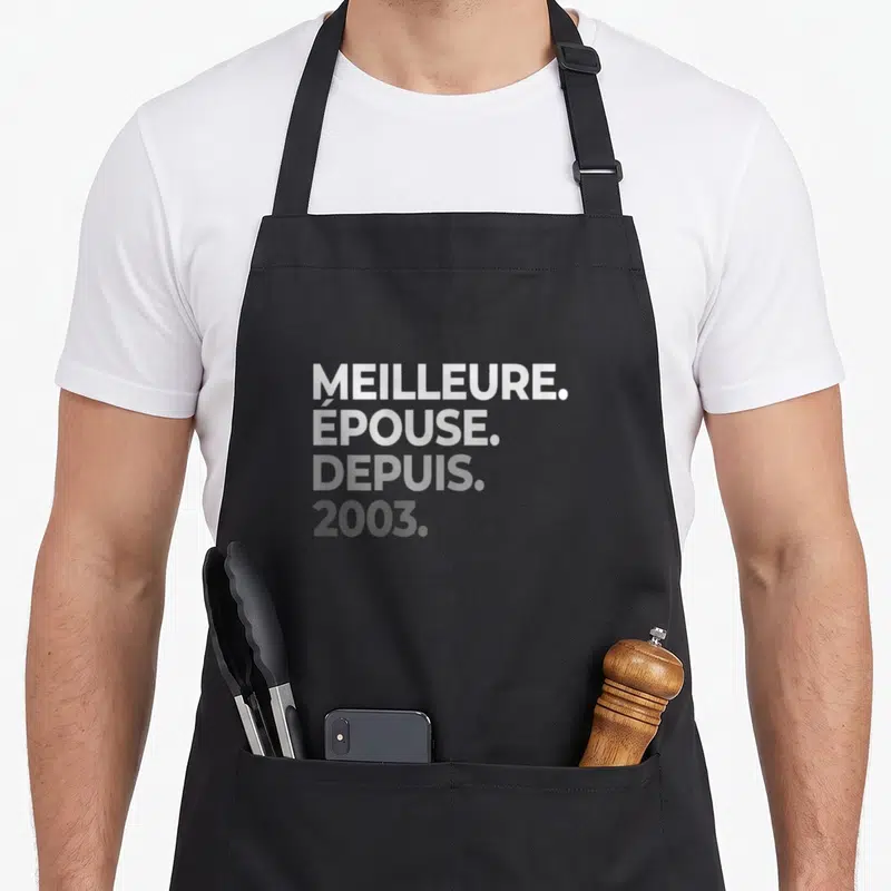 Tablier de cuisine noir avec l'inscription Meilleure Épouse Depuis 2003 en typographie blanche et grise.