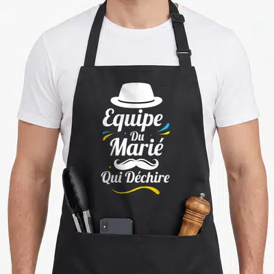 Tablier de cuisine noir avec le texte Equipe Du Marié Qui Déchire, une moustache stylisée et un chapeau blanc.