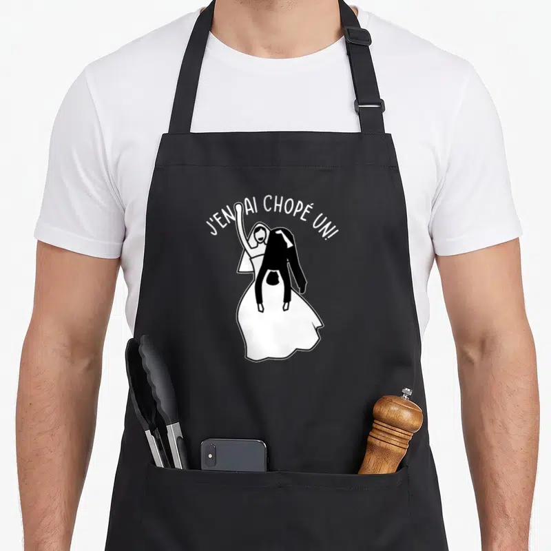 Tablier de cuisine noir avec une illustration d'un couple de mariés et le texte J'en ai chopé un.