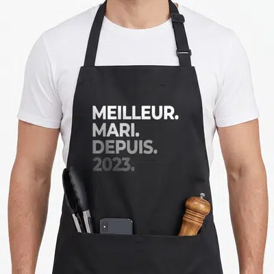 Tablier de cuisine noir avec l'inscription Meilleur Mari Depuis 2023 en lettres blanches et grises sur fond uni.