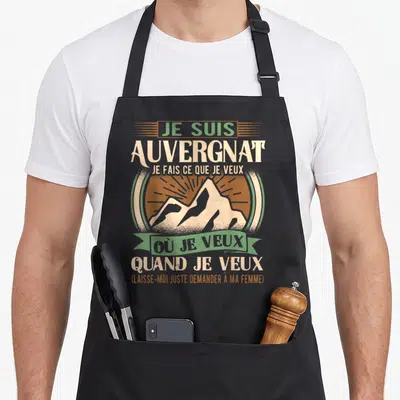 Tablier de cuisine noir avec une illustration de montagne et un texte humoristique sur l'autorité masculine en Auvergne.