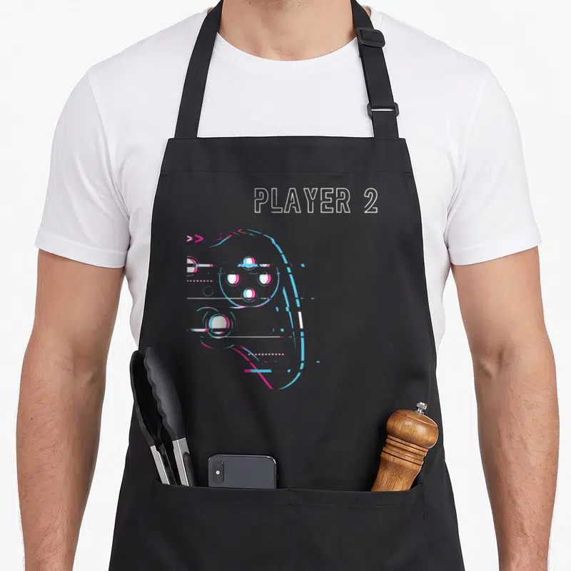 Tablier de cuisine noir avec illustration manette style glitch et texte blanc Player 2 en haut à droite.