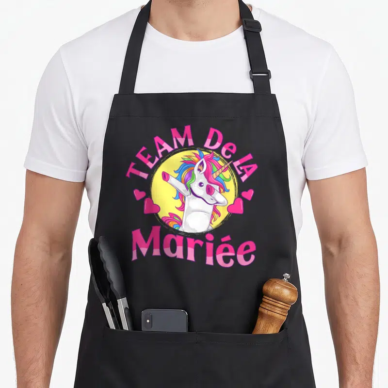 Tablier de cuisine noir avec licorne blanche aux cheveux multicolores effectuant un mouvement dab au centre d'un cercle jaune.