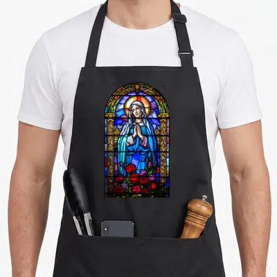 Tablier de cuisine noir avec un vitrail représentant la Sainte Vierge Marie en prière entourée de roses rouges et bleues.