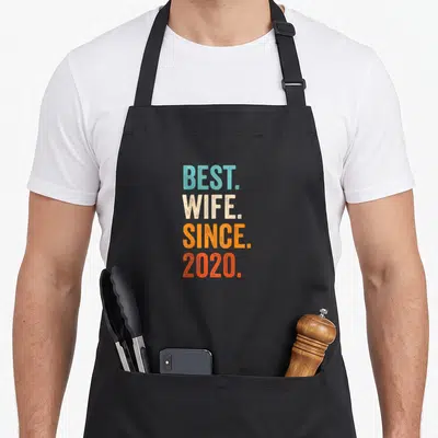 Tablier de cuisine noir avec le texte Best Wife Since 2020 en lettres capitales multicolores sur fond uni.