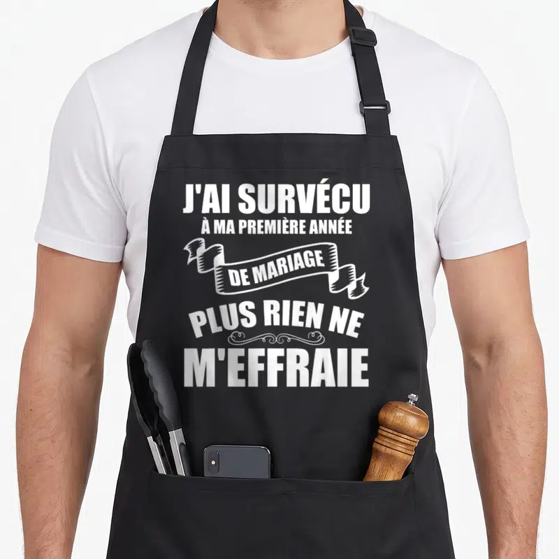 Tablier de cuisine noir avec inscription blanche J'ai survécu à ma première année de mariage plus rien ne m'effraie sur fond uni.