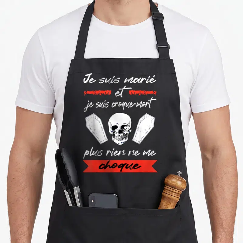 Tablier de cuisine noir avec un crâne central encadré de deux cercueils et du texte Je suis marié et je suis croque-mort plus rien ne me choque