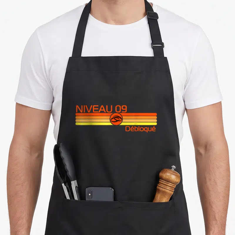 Tablier de cuisine noir avec graphique rétro orange et jaune indiquant niveau 09 débloqué sur fond uni.