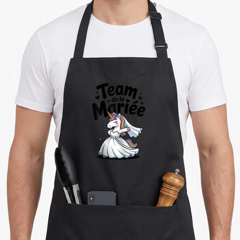 Tablier de cuisine noir avec une licorne en robe de mariée et le texte Team de la Mariée entouré de petits cœurs.