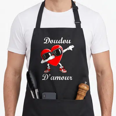 Tablier de cuisine noir avec un cœur rouge portant des lunettes et le texte Doudou D'amour.