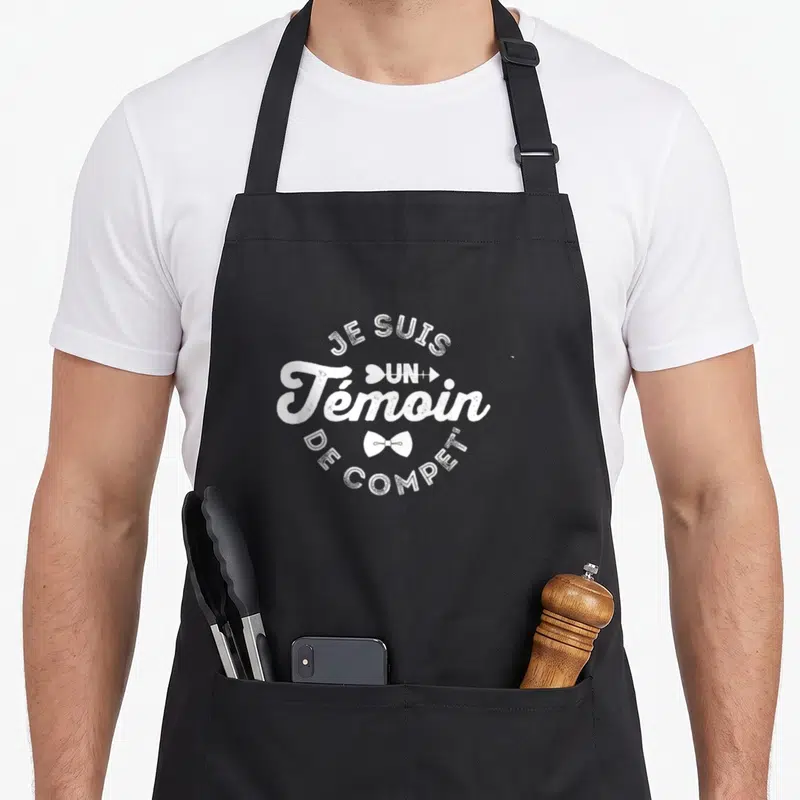 Tablier de cuisine noir avec inscription blanche Je suis un témoin de compét et des icônes de nœud papillon.