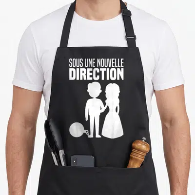 Tablier de cuisine noir avec silhouette blanche d'un couple et phrase sous une nouvelle direction illustrant l'enchaînement du mari.
