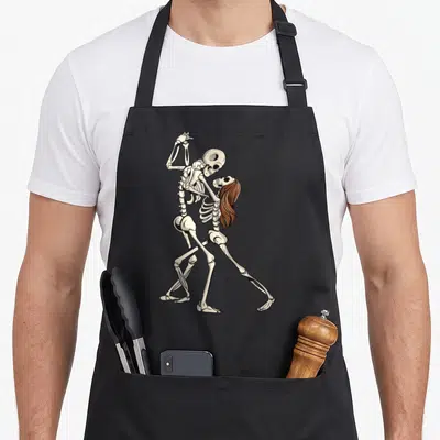 Tablier de cuisine noir avec deux squelettes s'embrassant en dansant, l'un aux longs cheveux bruns.