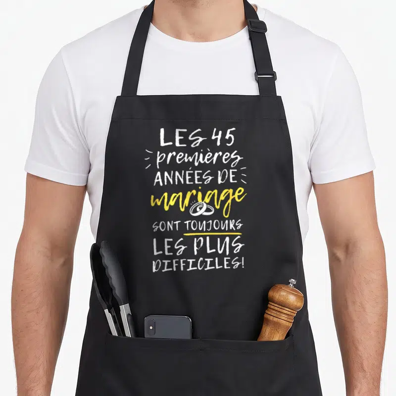 Tablier de cuisine noir avec texte blanc et jaune Les 45 premières années de mariage sont toujours les plus difficiles illustré par deux anneaux.