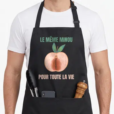 Tablier de cuisine noir avec illustration d'une pêche coupée et texte humoristique en deux couleurs.