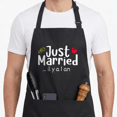 Tablier de cuisine noir avec linscription Just Married il y a 1 an et des anneaux dorés.