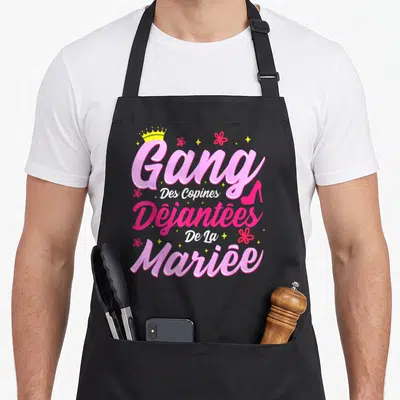 Tablier de cuisine noir avec le texte Gang Des Copines Déjantées De La Mariée en rose et jaune.