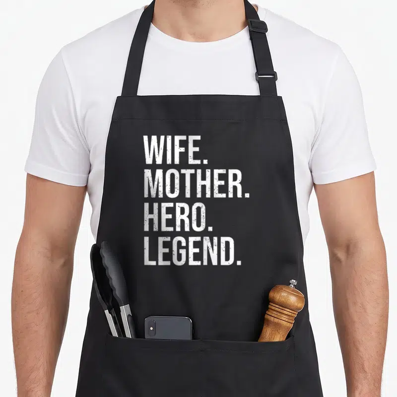 Tablier de cuisine noir avec l'inscription Wife Mother Hero Legend en lettres blanches verticales.