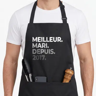 Tablier de cuisine noir avec le texte Meilleur Mari Depuis 2017 imprimé en blanc et gris sur le devant.