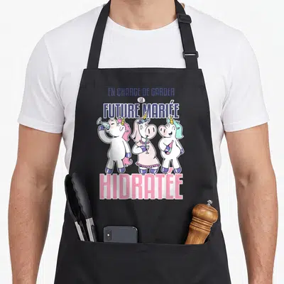 Tablier de cuisine noir avec trois licornes colorées et le texte En charge de garder la future mariée hidratée imprimé en haut et en bas.