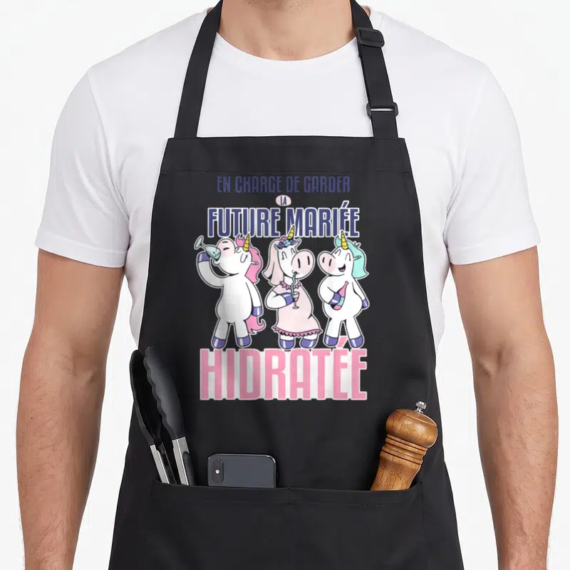 Tablier de cuisine noir avec trois licornes colorées et le texte En charge de garder la future mariée hidratée imprimé en haut et en bas.