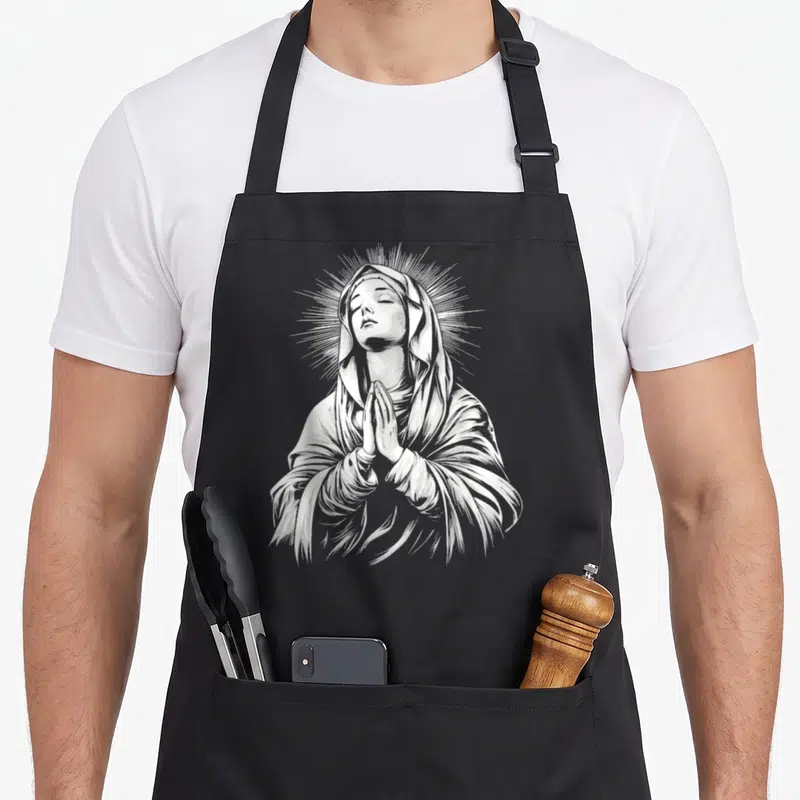 Tablier de cuisine noir avec une illustration blanche de La Bienheureuse Vierge Marie en prière et un halo rayonnant.