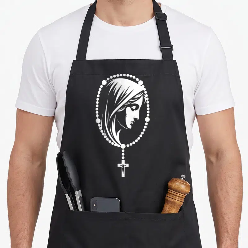 Tablier de cuisine noir avec illustration blanche d'un rosaire encadrant le visage de la Vierge Marie et un crucifix en bas.