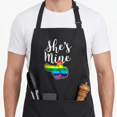 Tablier de cuisine noir avec inscription She Is Mine et main colorée pointant vers le côté