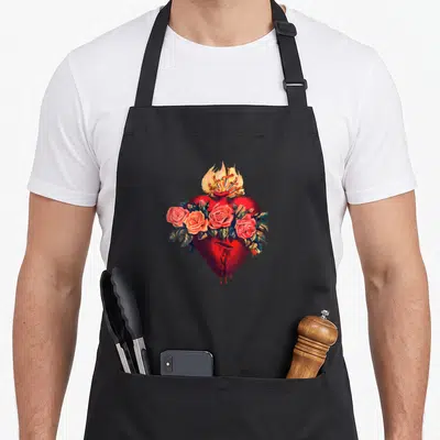Tablier de cuisine noir avec un cœur rouge entouré de roses et surmonté de flammes dorées.