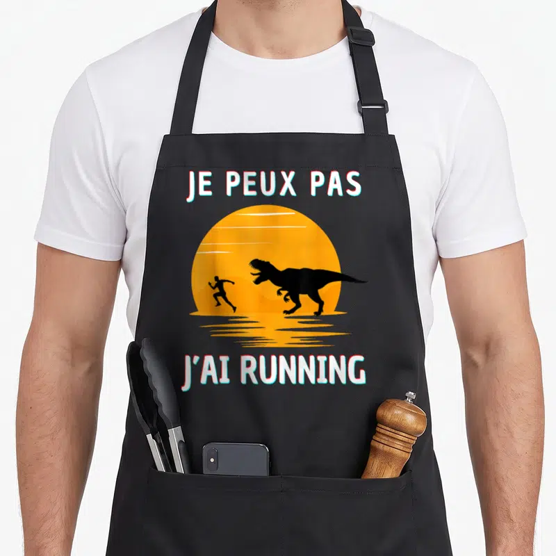 Tablier de cuisine noir avec une illustration d'un homme fuyant un dinosaure sous un soleil orange et le texte Je peux pas j'ai running.