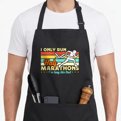 Tablier de cuisine noir avec illustration d'un coureur et texte I Only Run Half Marathons sur fond de bandes colorées rétro.