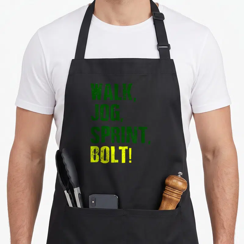 Tablier de cuisine noir avec le texte vert et jaune « WALK, JOG, SPRINT, BOLT! » imprimé au centre.