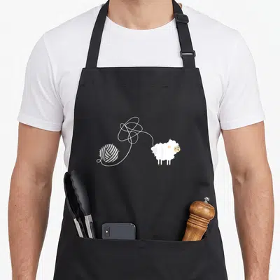 Tablier de cuisine noir avec illustration d'un mouton blanc et d'une boule de fil blanc tracée en ligne fine.