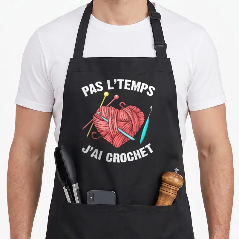Tablier de cuisine noir avec une bobine de fil rose en forme de cœur et des crochets colorés.