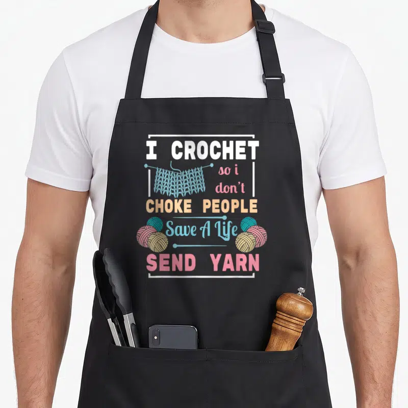 Tablier de cuisine noir avec texte I Crochet Save A Life Send Yarn et illustrations de pelotes de laine.